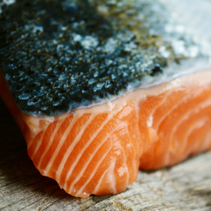 Sensitive StomachClose-up of a raw salmon fillet on a wooden surface, showcasing its vibrant orange color and textured scales, conveying freshness and quality.